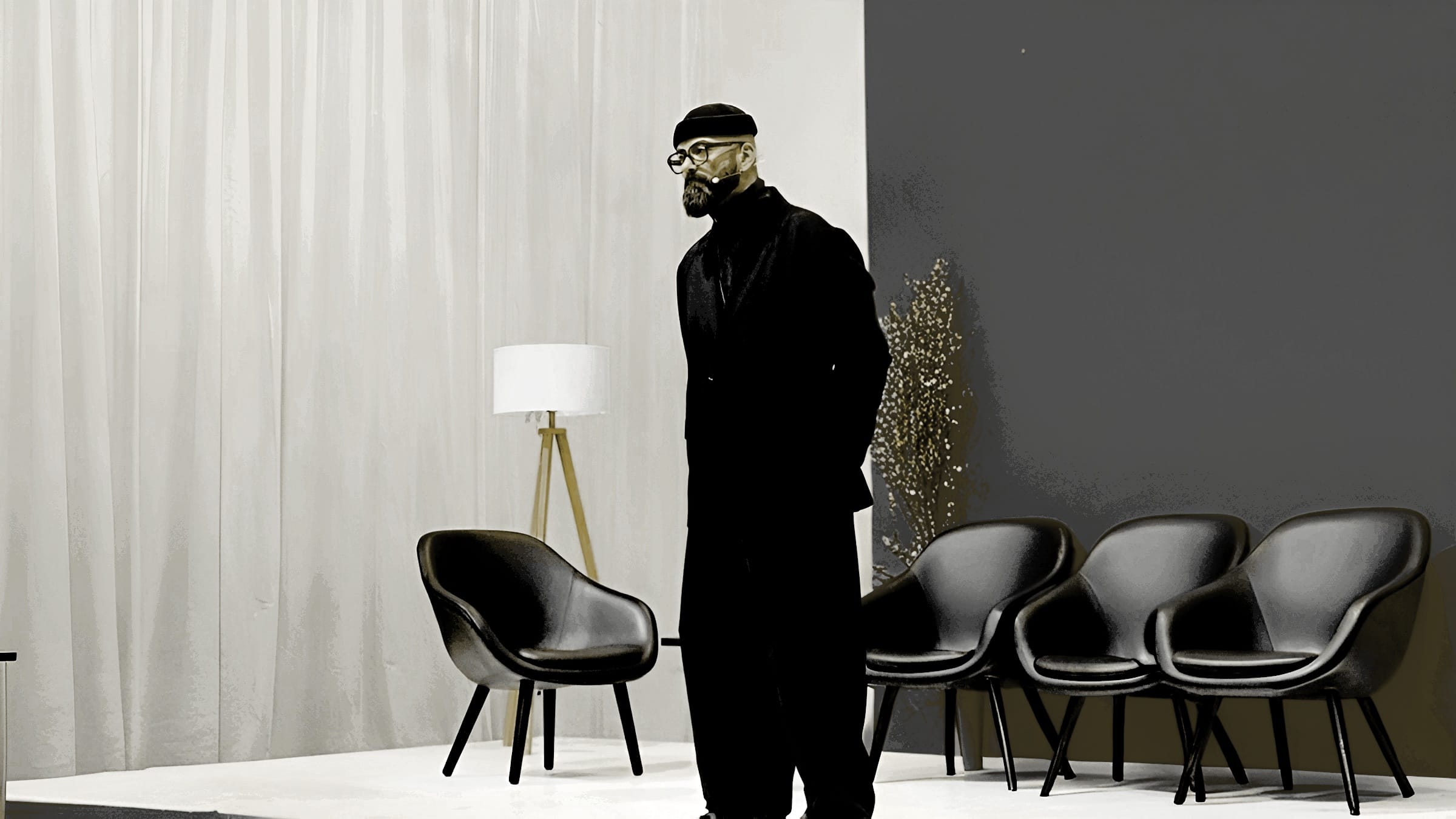 ERDBEERSCHNITTE Cihan Bulut Friseursalon 2.0 - stylischer Mann in schwarzem Outfit vor Designerstühlen